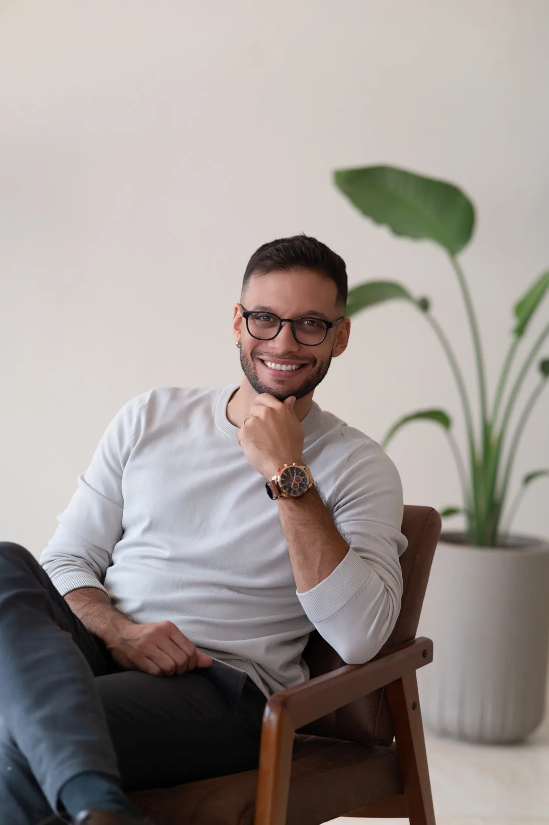 Henrique Costa sorrindo, sentado em uma poltrona de madeira